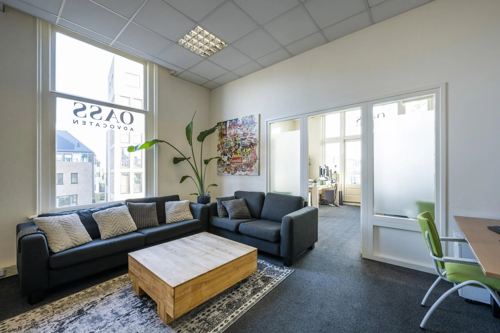 Modern ingerichte wachtruimte van advocatenkantoor Oass aan de Van Eedenstraat met comfortabele zitbanken en een lage houten tafel.